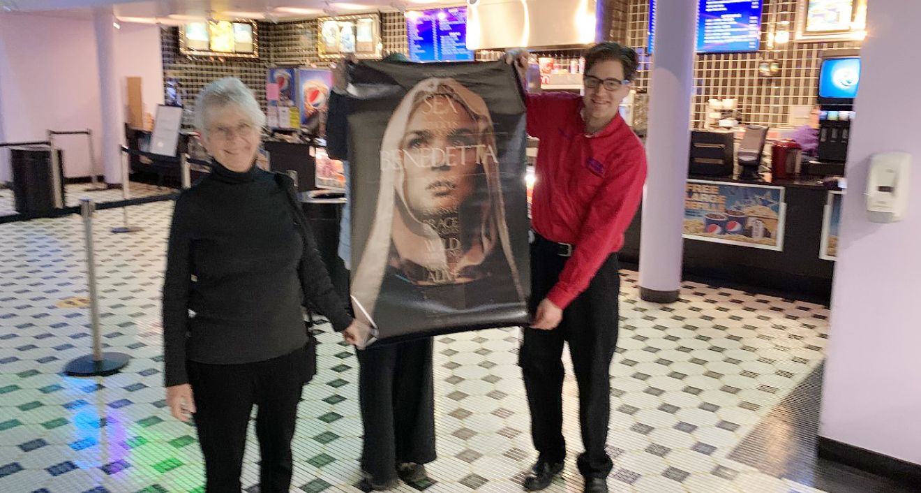 Judith Brown, at left, holds a poster advertising the film, Benedetta.