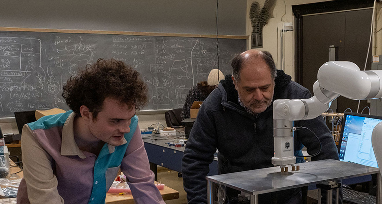 Adin Dowling ’25 (left) and Lauren B. Dachs Professor of Science and Society Tsampikos Kottos (right) operate a robotic arm. (Photo by Mike Mavredakis)
