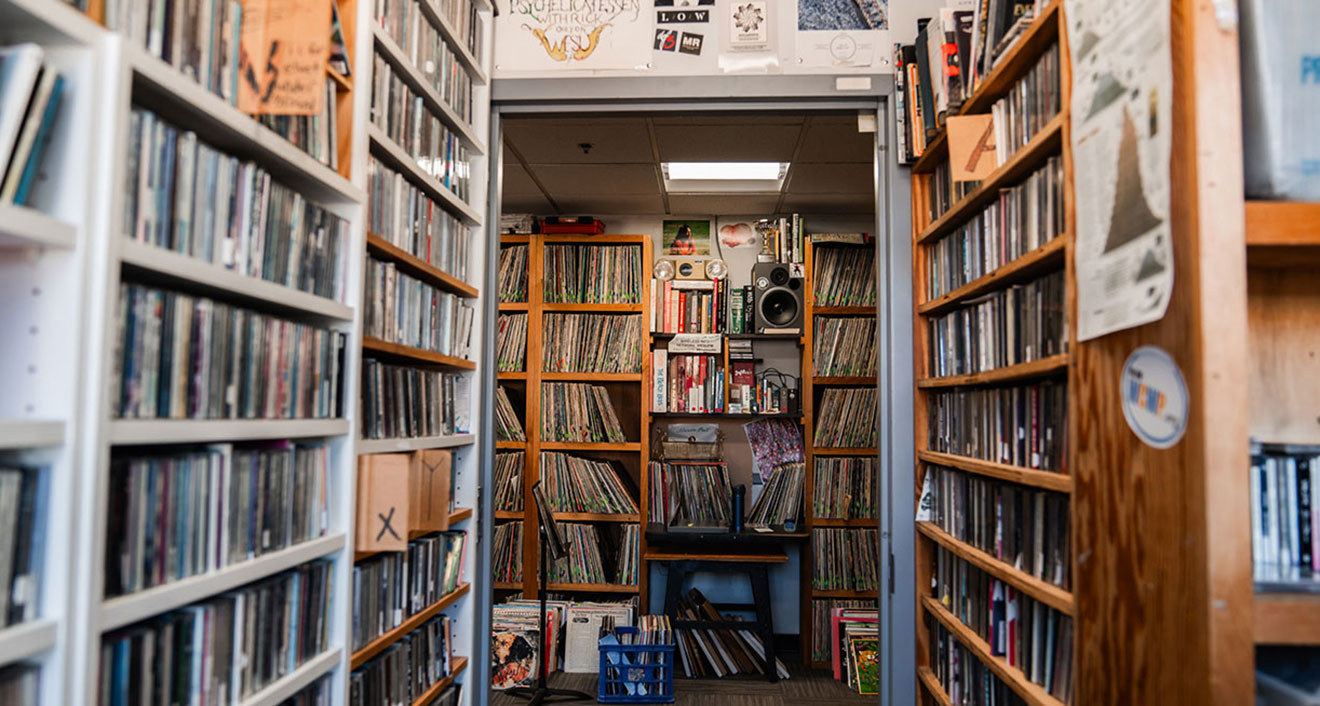 The shelves at WESU are stuffed with music and the walls are plastered with stickers and posters. (Photo by Meka Wilson)