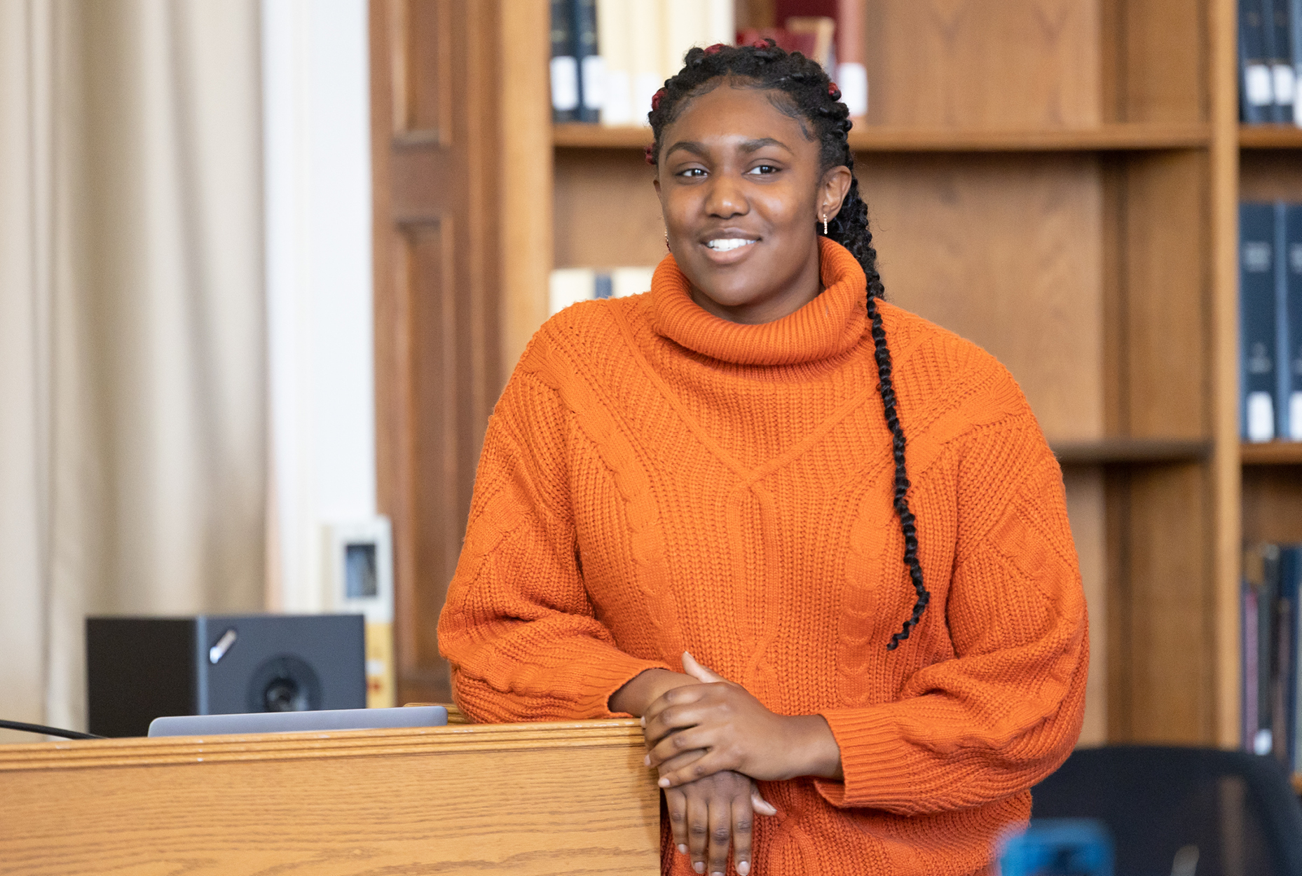 Student speaking at podium with bookshelves in background 
