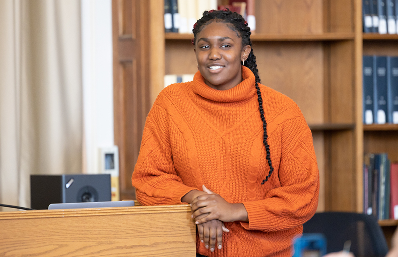 Student speaking at podium with bookshelves in background 