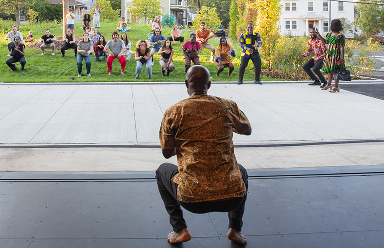 Dancer on stage viewed from behind teaching dance moves to audience on lawn