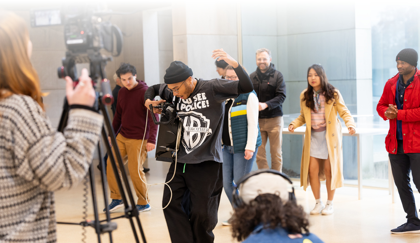 Videographers documenting artist leading audience in movement in gallery    