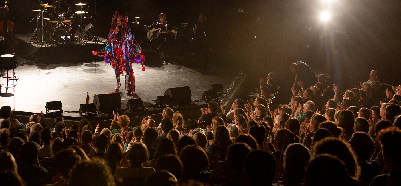 Performer on stage with musicians in front of seated audience