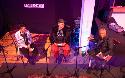 Three artists talking to audience with a curtain behind and a sign that says “FREE CNTR”