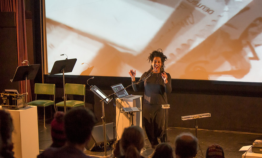 Artist speaking to audience with image projected on screen behind
