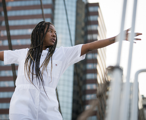 Dancer on boat with rigging lines in front and buildings in background 