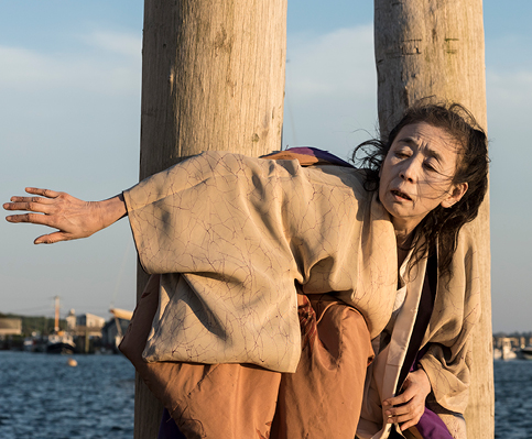 Dancer on dock with wooden pilings and ocean behind 