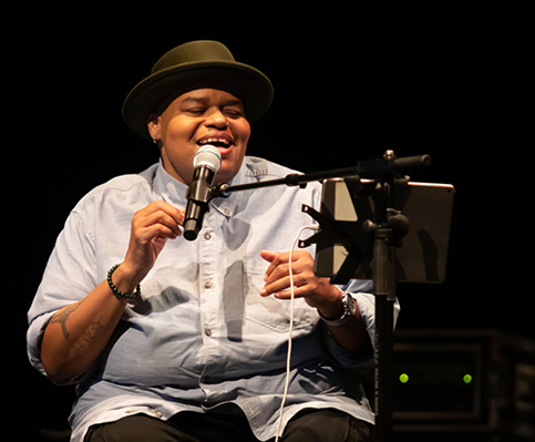 Musician wearing hat seated and singing in front of microphone 