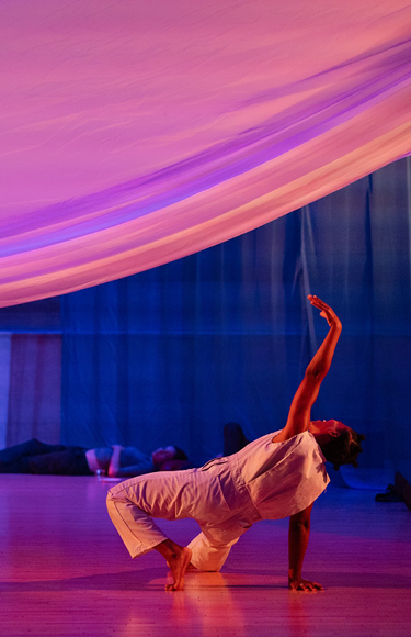 Dancer moving under large sheet with other people lying on floor and sitting against back wall - mobile version