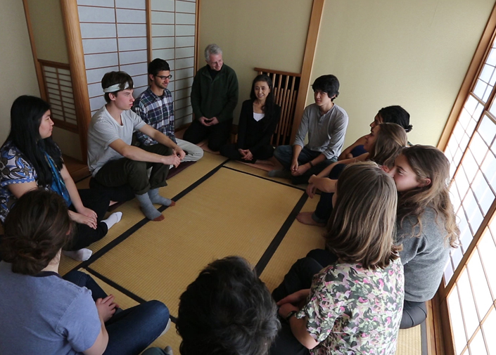 Three recycling and waste containers with two people standing behind them and tents and river in background