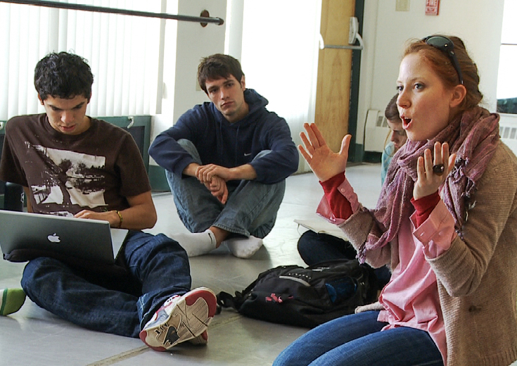 Seated artist talking to class with students taking notes 