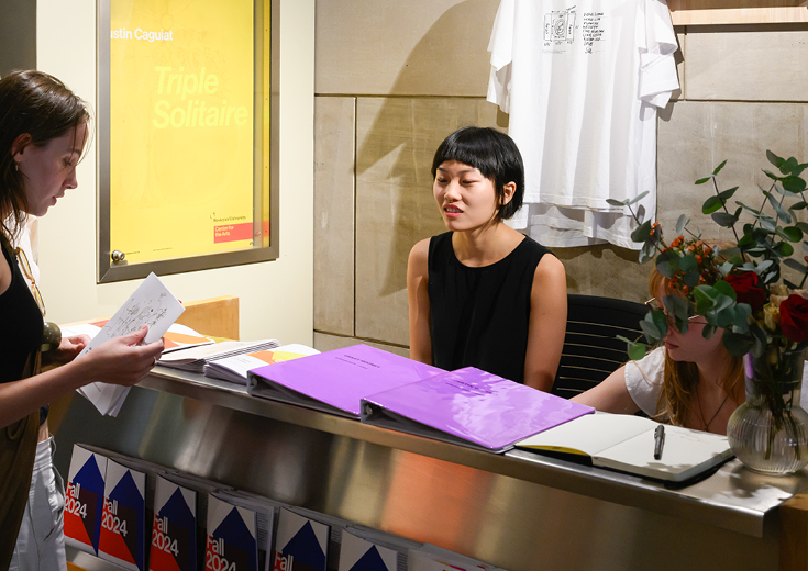 Gallery monitors behind desk covered with gallery literature with visitor browsing materials