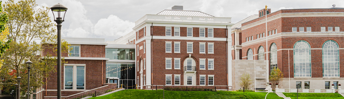 Brick and limestone buildings with grass and trees and lamppost in foreground 