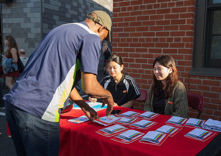 Two seated students assist visitor at outside table with programs 