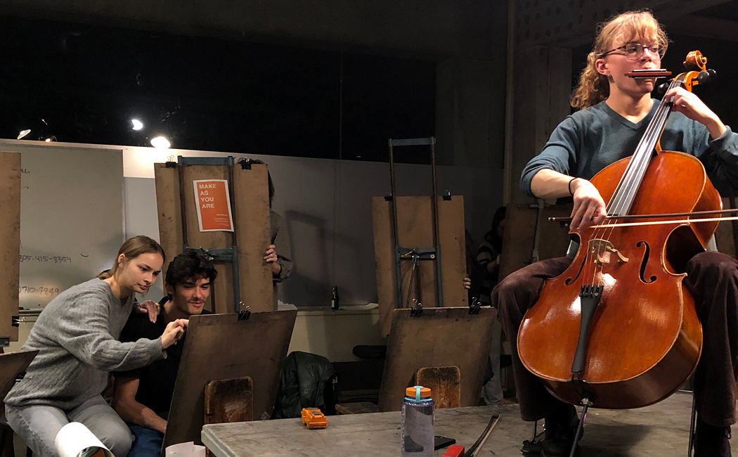 Two students drawing musician on platform with cello and harmonica 