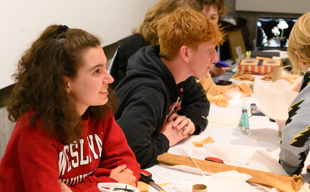 Students seated at table with paper and glue guns assisting visitors with project