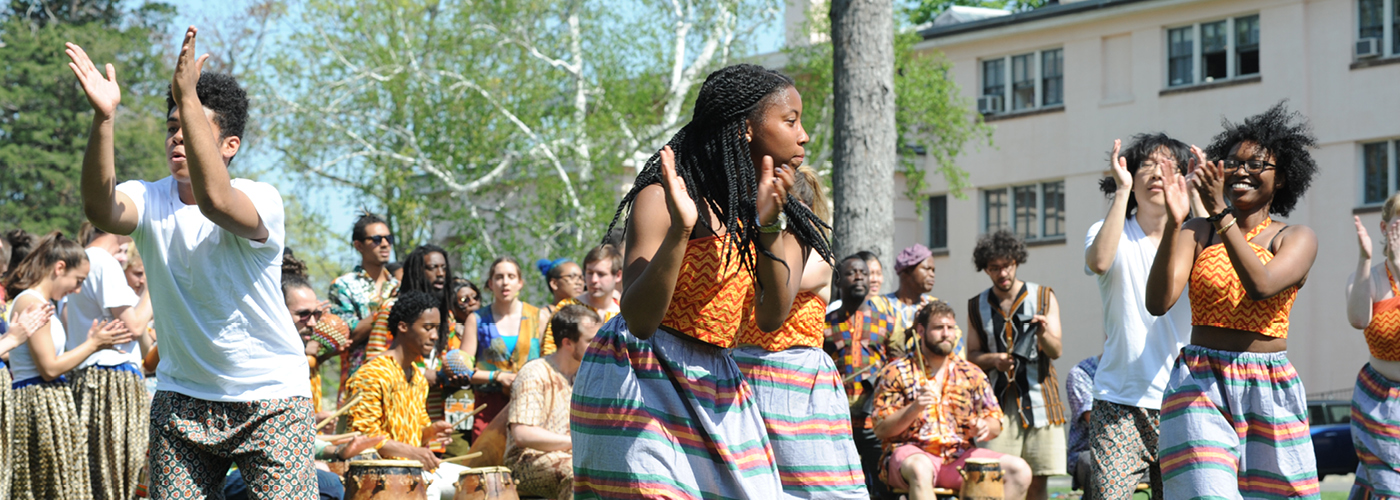 Students dancing outside with drummers and trees behind them 