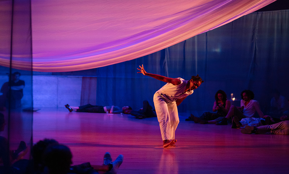 Person bending toward floor with one hand reaching up to cloth above with others in background