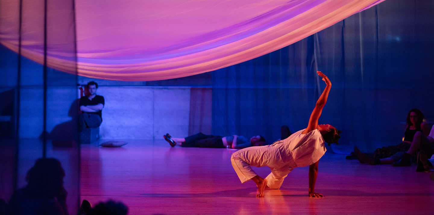 Dancer moving under large sheet with other people lying on floor and sitting against back wall 