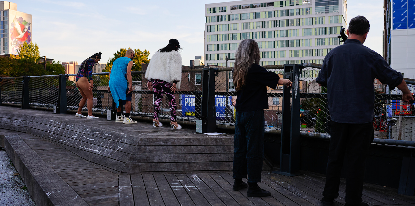 People seen from behind in front of fence on rooftop looking down at street 