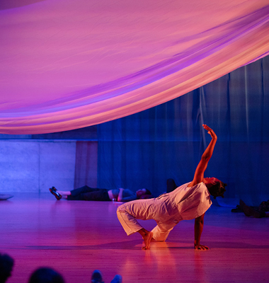 Dancer moving under large sheet with other people lying on floor and sitting against back wall
