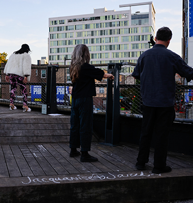People seen from behind in front of fence on rooftop looking down at street