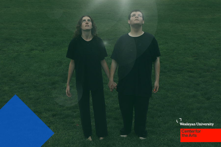 Two people on lawn at night looking upward toward light