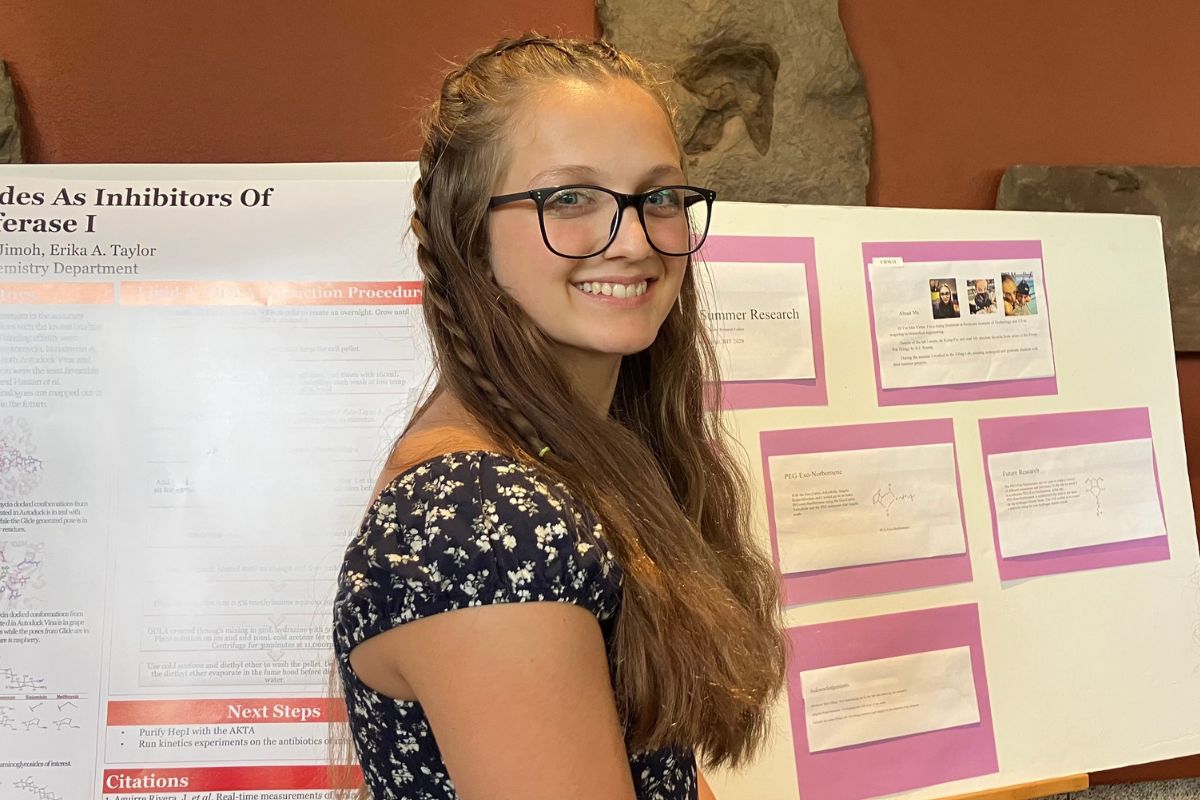 a young woman smiles beside scientific poters